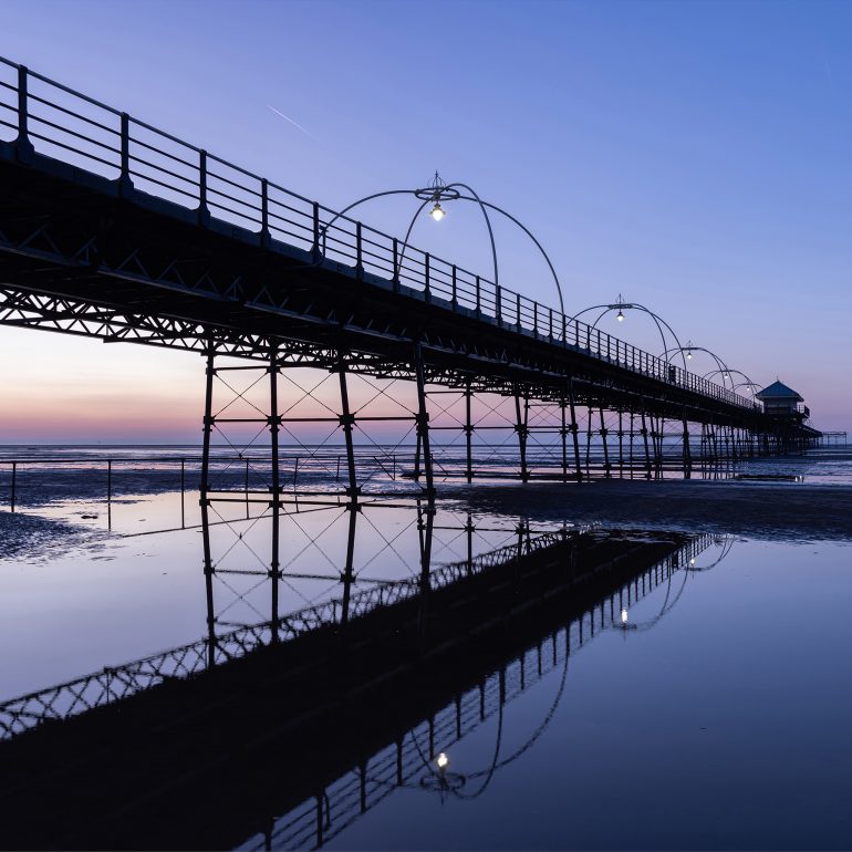 Cools blues and pinks sunset from the beach next to Southport pier Merseyside, north west UK coast beach, with reflections and shadows of the pier in the water under the pier