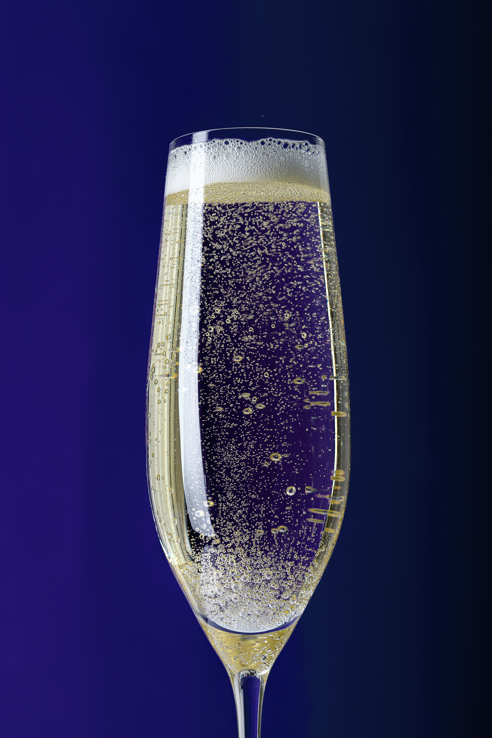 Drinks photographer, drinks photography Champagne in a flute glass with bubbles on a blue background