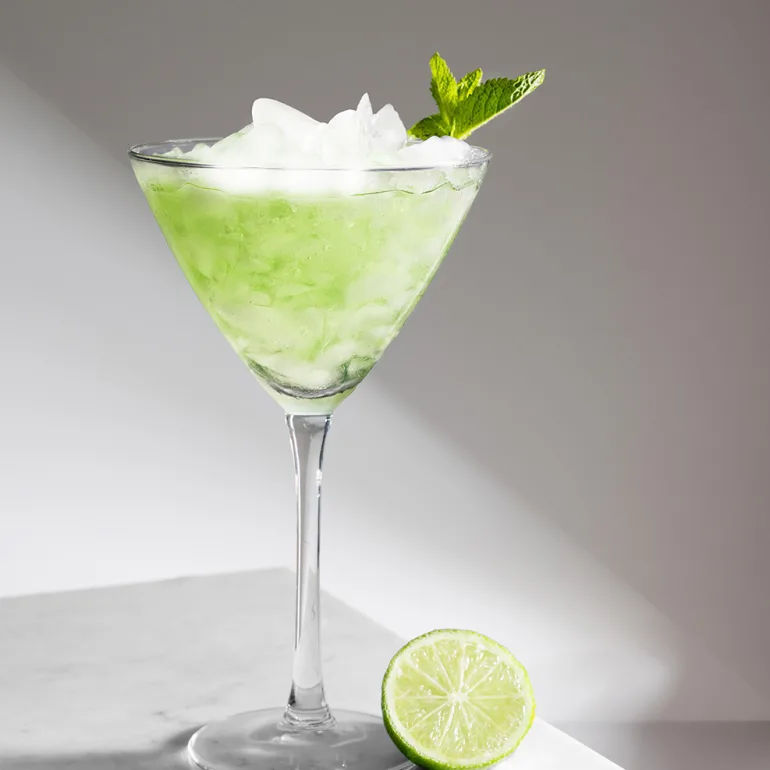 Green cocktail in a martini glass with strong shadows on a white background